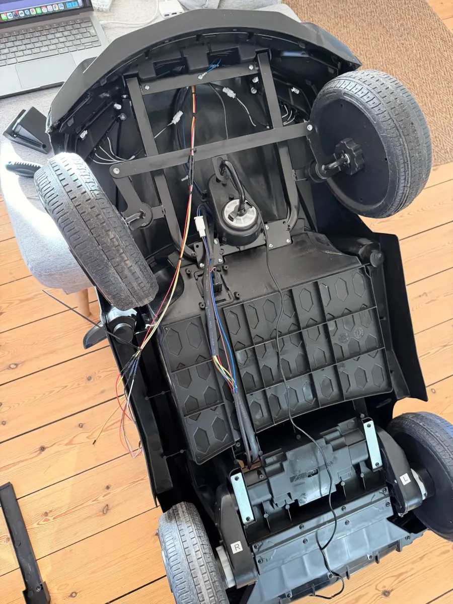The ride-on car stripped to its chassis, showing the wiring loom and drive motors